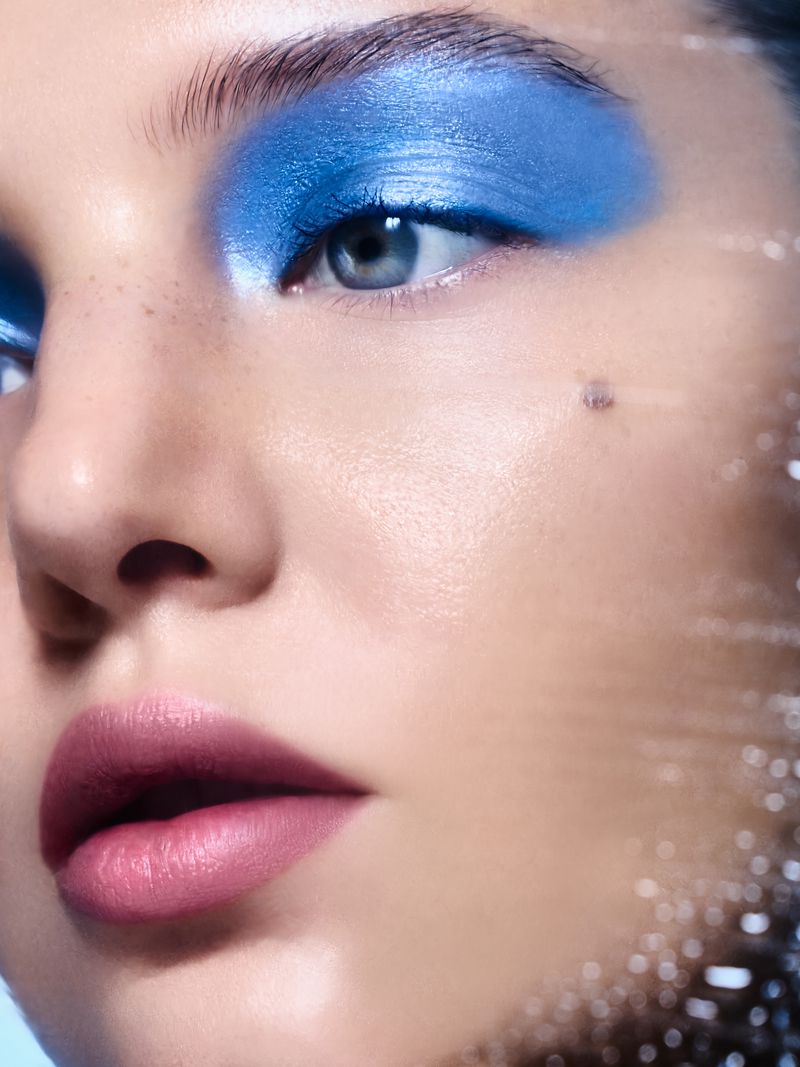 Close-up portrait of a fair-skinned woman with vivid blue eyeshadow and pink lipstick, showcasing beauty and cosmetic artistry.