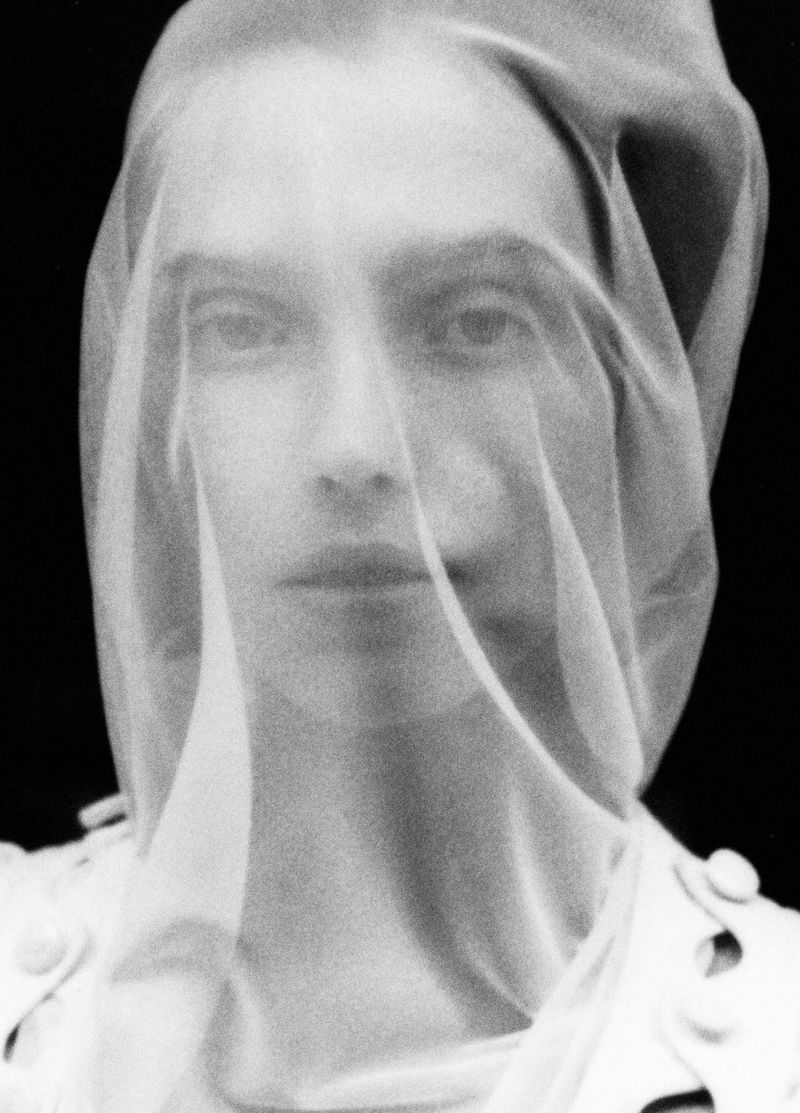 Close-up portrait of an adult woman wearing a sheer white veil in a black and white photograph with shallow depth of field.