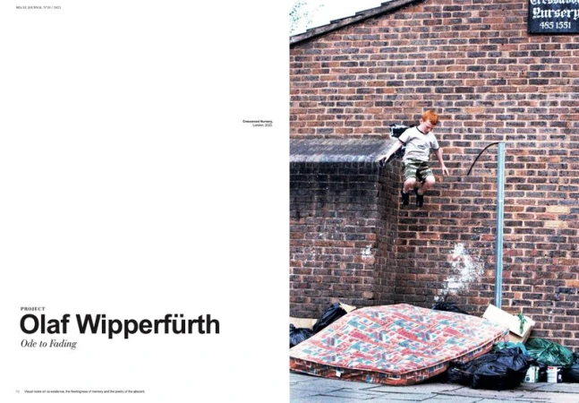 Boy in mid-air leaping off brick wall, with mattress and trash below. Bright red hair and blurred motion accent youthful energy.