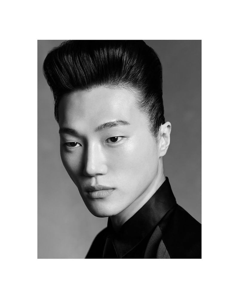 Striking black and white portrait of an Asian male model with slicked-back hair, wearing a dark collared shirt against a grey backdrop.