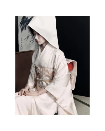 Woman in traditional Japanese wedding kimono and wataboshi hood, seated against a black background with a crane painting visible.