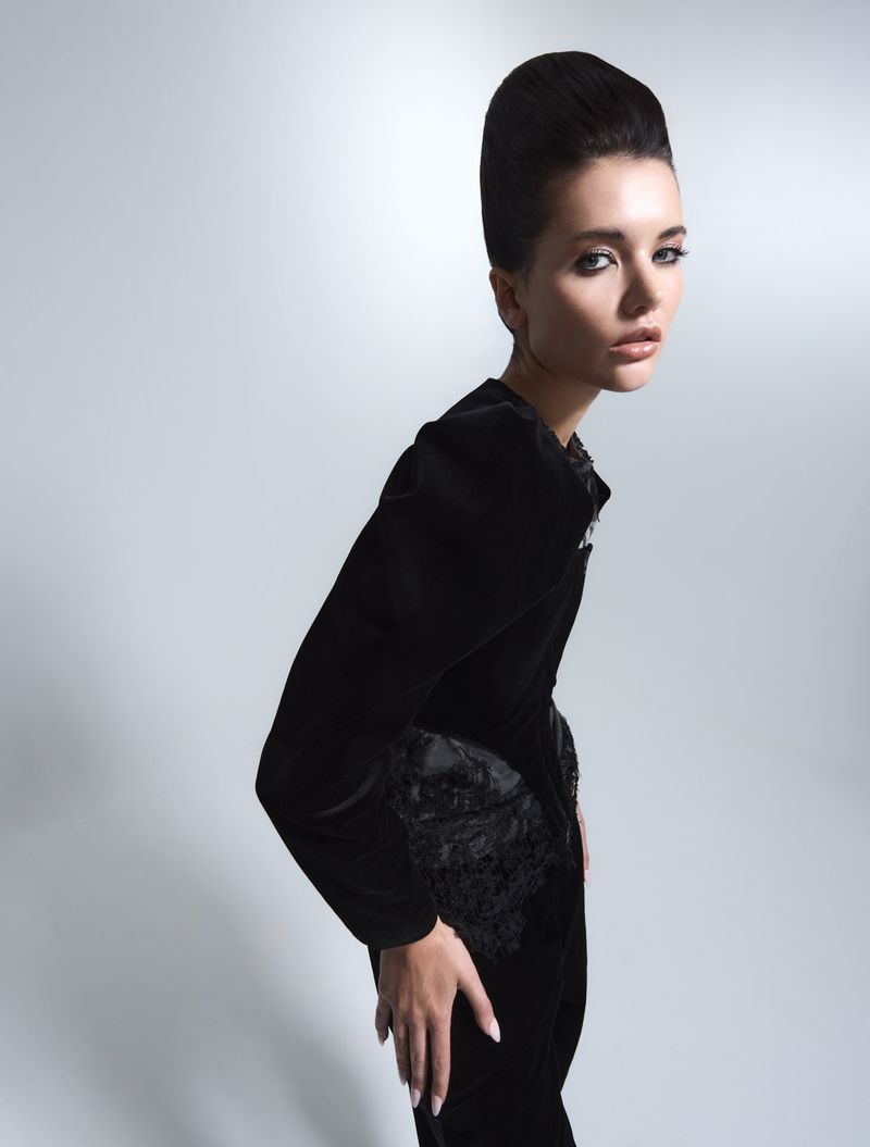 Elegant woman in black velvet dress with updo hairstyle, posed in a light studio setting, fashion photography.