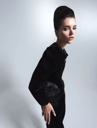 Elegant woman in black velvet dress with updo hairstyle, posed in a light studio setting, fashion photography.
