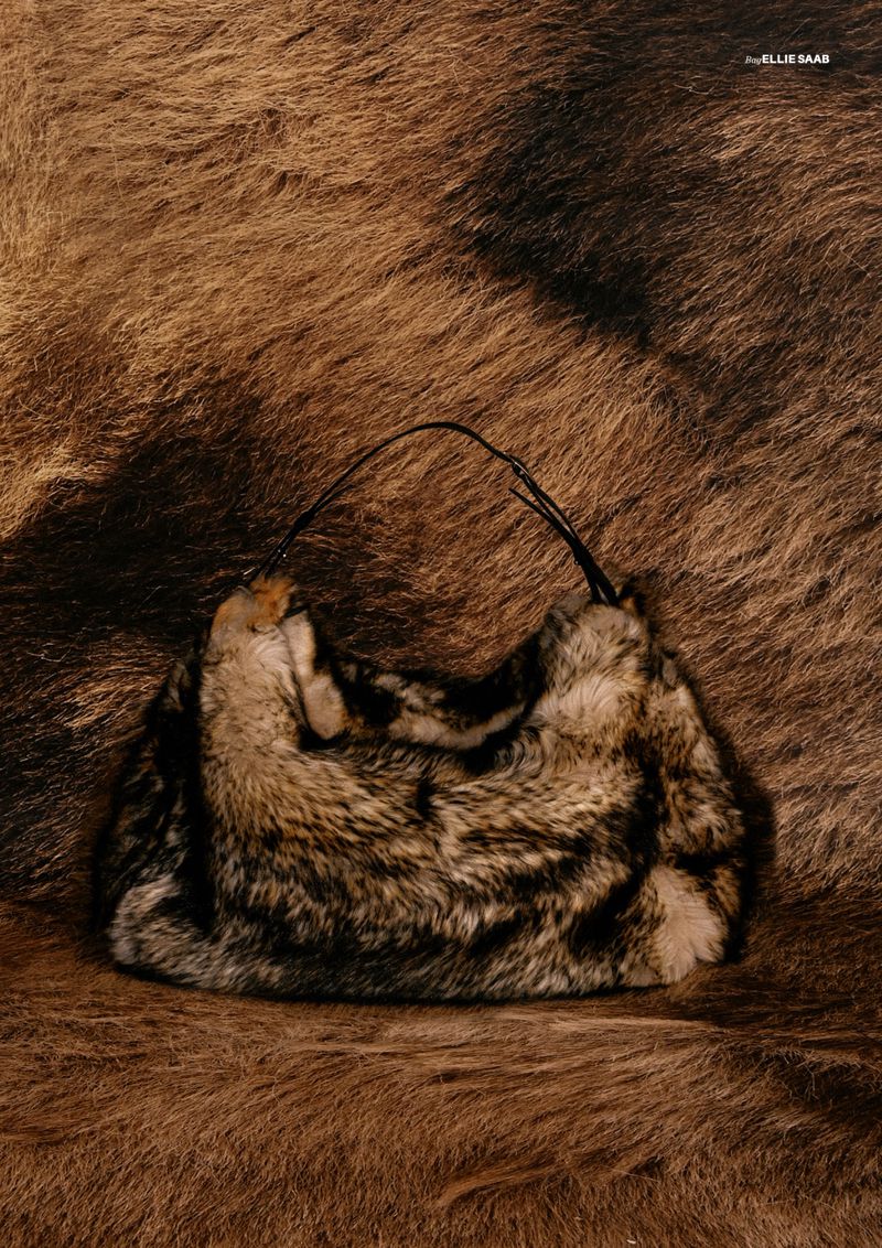Fur handbag with black straps sits on a brown fur background. The lighting is soft and warm, and the texture is emphasized.
