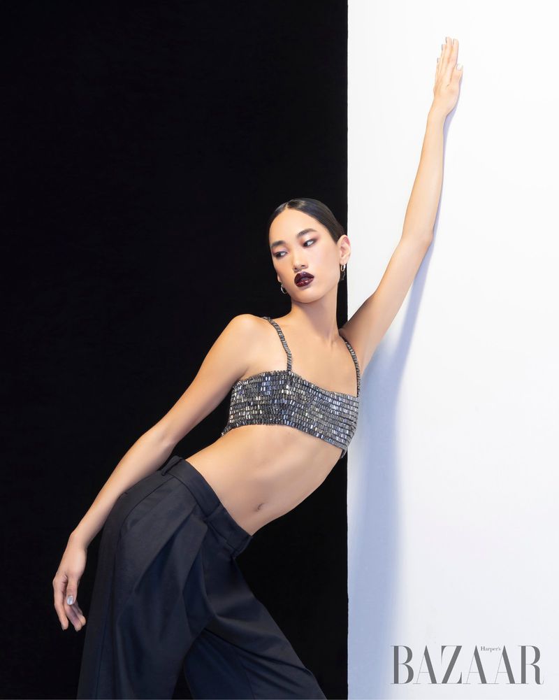 Fashion shot of an Asian woman in a sequined crop top and black pants posing against a black and white background, beauty editorial.