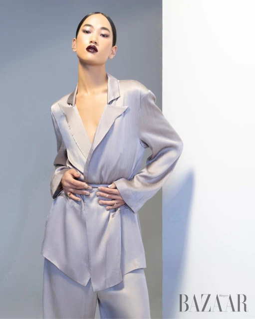 Elegant Asian woman in a modern silver blazer and matching wide-leg trousers poses in a fashion shot against a grey-white studio backdrop.
