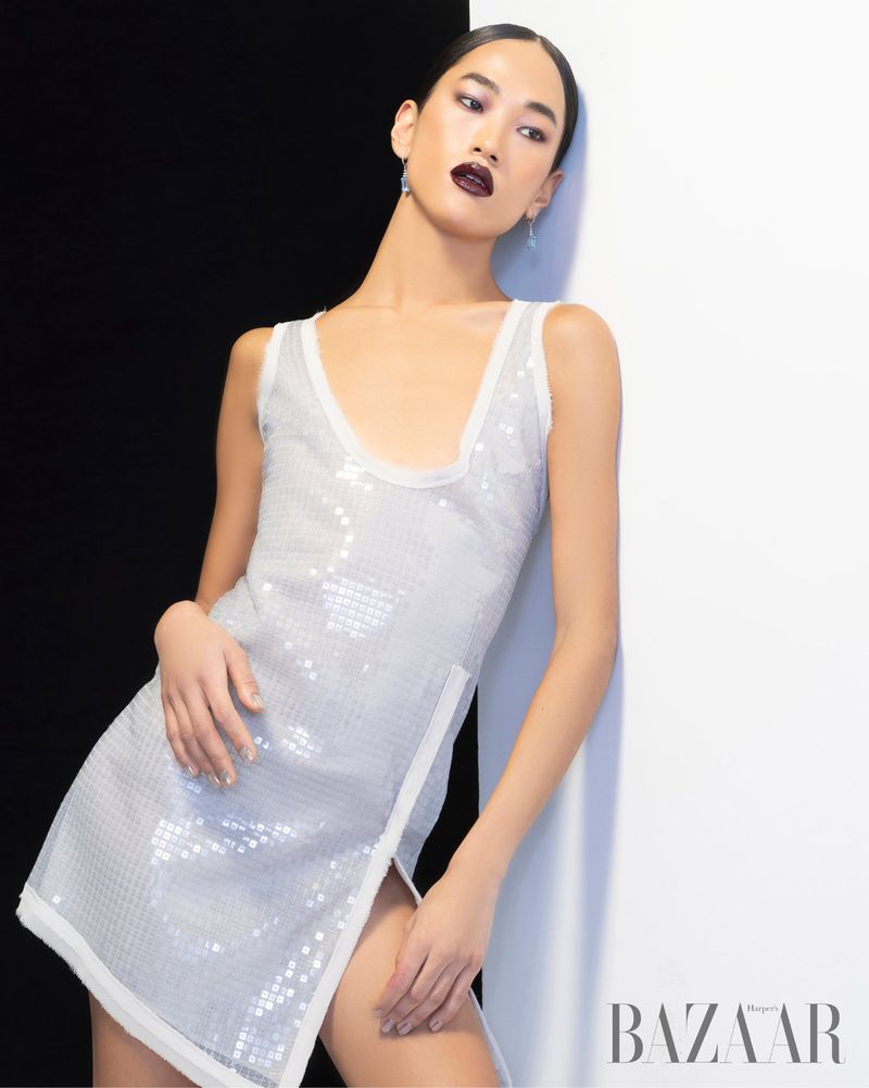 Elegant Asian woman in sequin dress poses against black and white background. Fashion editorial shot with soft lighting, wearing dark lipstick.