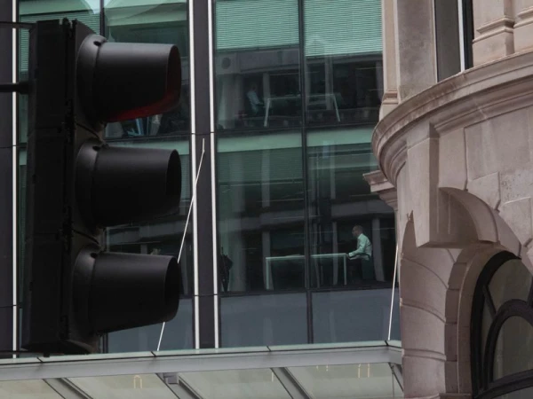 Urban scene featuring a black traffic light in the foreground with modern office building behind and traditional stone building.