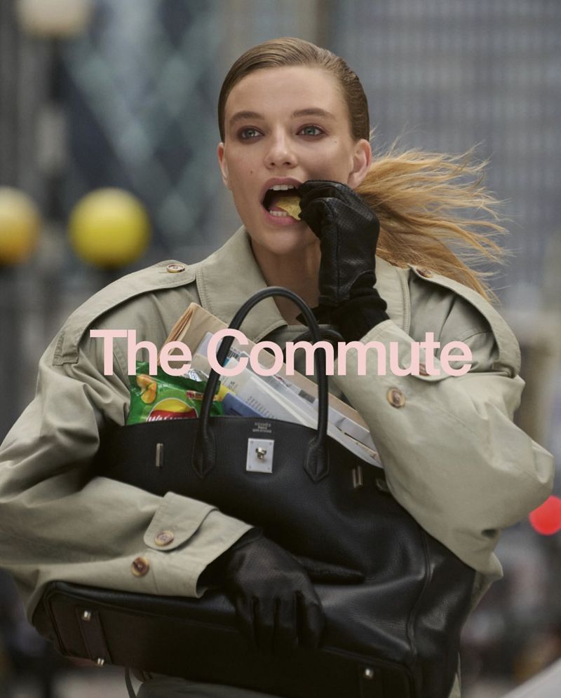 A blonde woman in a trench coat eats a snack from a black leather purse in an urban setting, showcasing fashion and everyday life.