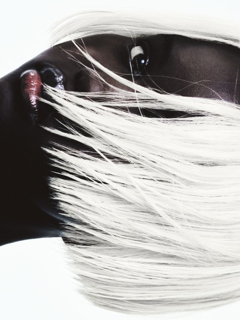 Glamour headshot of a woman with dark skin and flowing platinum blonde hair, showcasing beauty and style against a white background.