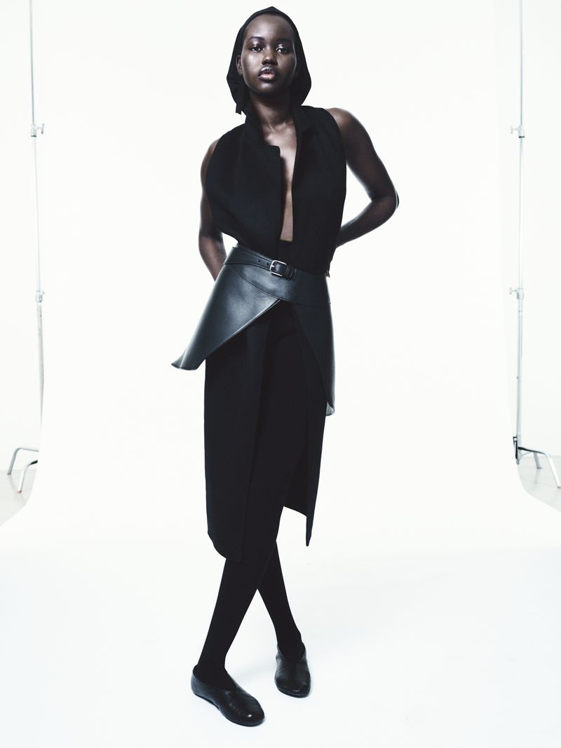 Elegant studio shot of a Black female fashion model in black sleeveless top, pants, leggings and shoes, wearing a black leather belt.