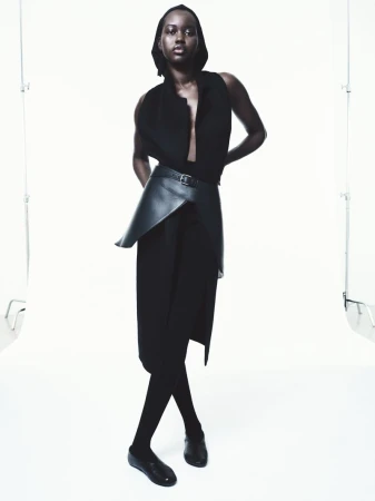 Elegant studio shot of a Black female fashion model in black sleeveless top, pants, leggings and shoes, wearing a black leather belt.