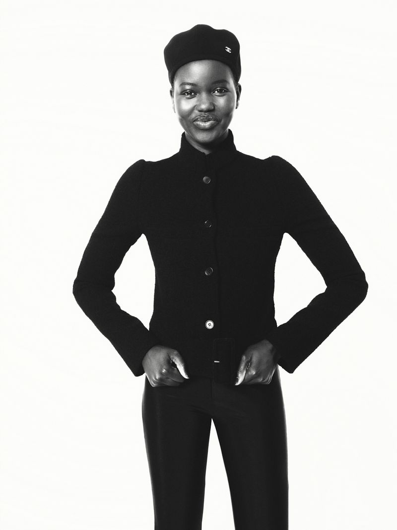 Elegant portrait of a Black woman in a dark beret and black suit jacket, set against a stark white backdrop in a studio environment.