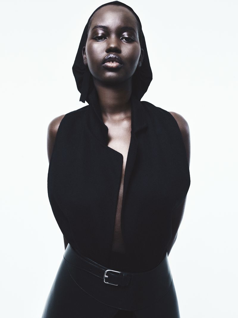 Portrait of an African woman with a hooded collar in a sleeveless jacket and black leather pants in a photo studio on a white background.