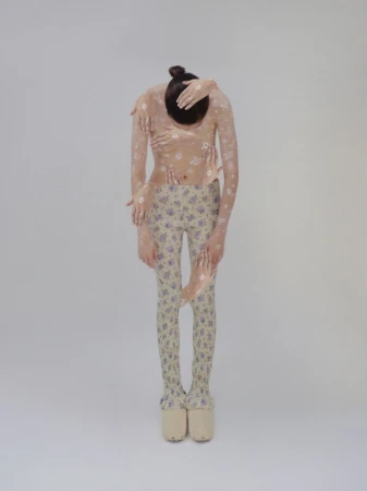 Full-length portrait of an androgynous figure covered in a floral pattern and multiple arms, wearing platform shoes on a white backdrop.