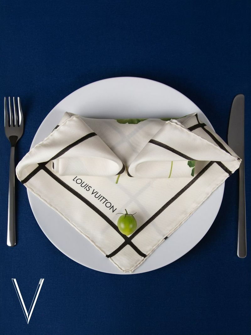 Elegant place setting featuring a Louis Vuitton napkin on a plate with silverware on a blue background, stylish and sophisticated design.