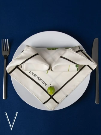 Elegant place setting featuring a Louis Vuitton napkin on a plate with silverware on a blue background, stylish and sophisticated design.