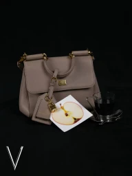 Taupe leather handbag with gold hardware next to an apple print card and an espresso cup on a black surface.