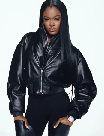 Black woman wearing a black leather puffer jacket and dark trousers against a white seamless background.