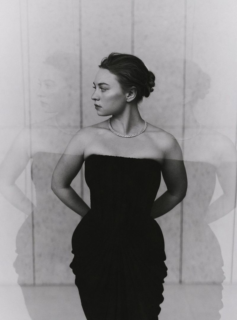 Monochrome portrait of a woman in a black strapless dress and necklace looking to the side with a blurred double exposure effect.