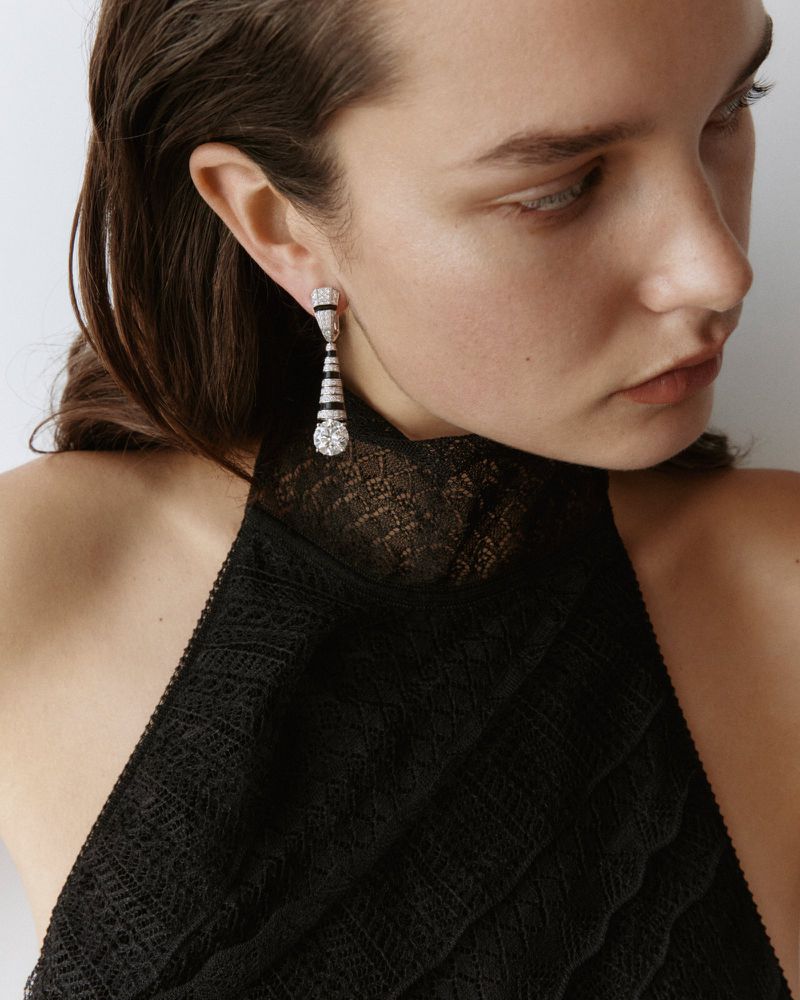 Model wearing diamond and black dangle earrings and a black lace top in a studio setting with a soft, diffused lighting scheme.