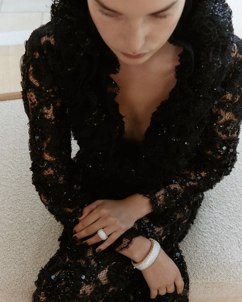Model wearing a black lace dress with white beaded ring and bracelet in high-angle view