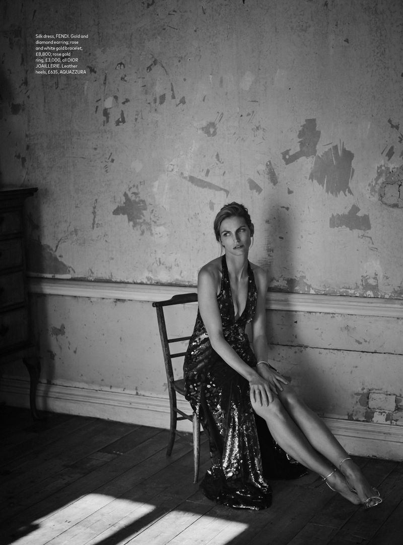 A woman in an elegant gown sits on a chair in a distressed interior, bathed in light highlighting the textures of the room and her attire.