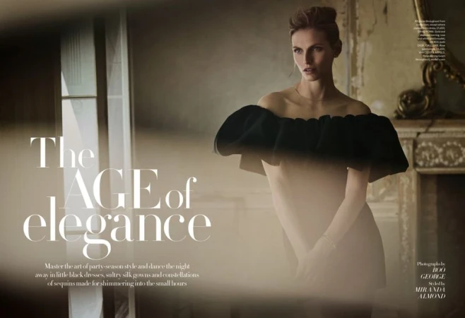 Elegant fashion shot of a woman in an off-the-shoulder black ruffled dress, posing in front of a textured wall with an antique fireplace.