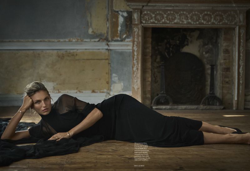 Indoor fashion shot featuring a blonde woman in a black dress, lying on a wooden floor in a distressed vintage interior with a fireplace.