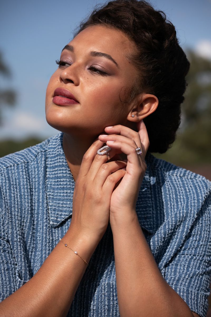Portrait of a woman wearing a blue textured top and rings, looking upward outdoors.
