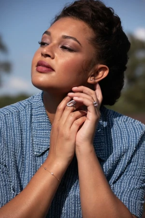Portrait of a woman wearing a blue textured top and rings, looking upward outdoors.