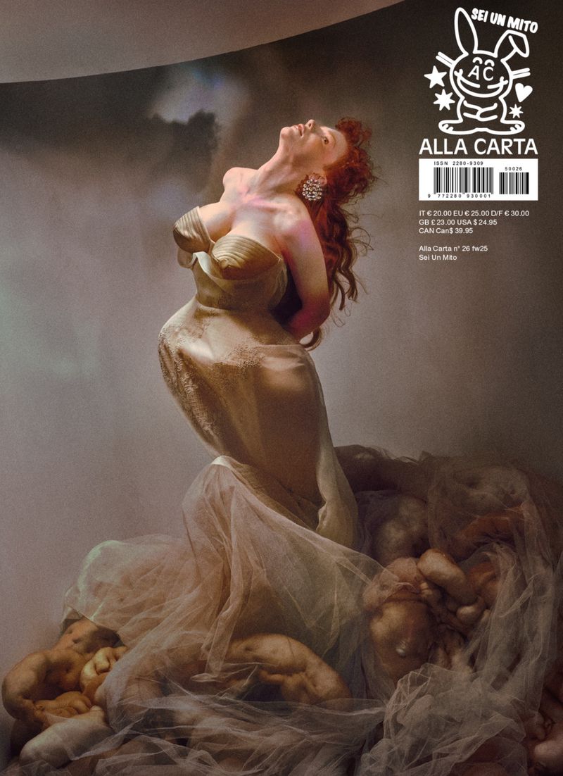 Magazine cover featuring a woman in a draped gown with red hair, looking up, surrounded by abstract figures and dramatic lighting.
