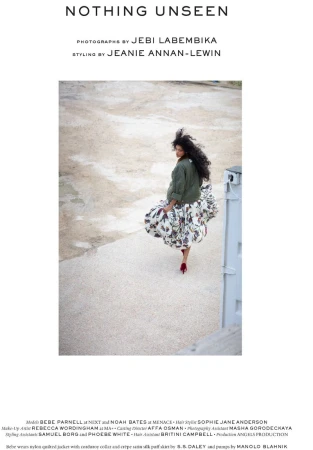 A woman with curly dark hair dances in a floral dress and red heels, outdoors on a stone surface in natural lighting.