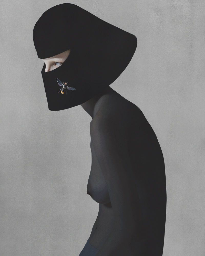 Artistic portrait of a woman with a black head covering adorned with an insect brooch, set against a plain gray backdrop.