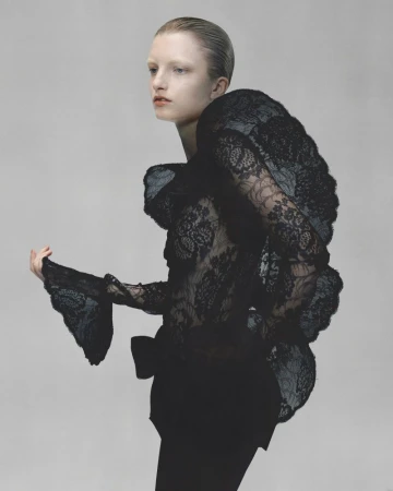 Model Kristin Drab in profile wearing an avant-garde black sheer floral lace top against a soft grey studio seamless backdrop.
