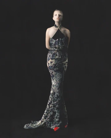 Model Kristin Drab in a floor-length printed halter gown posing against a solid black backdrop with red shoes visible at the hem.