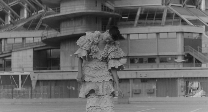 Model Nat Veil wearing a sculptural tiered ruffle dress in front of brutalist concrete architecture in black and white.