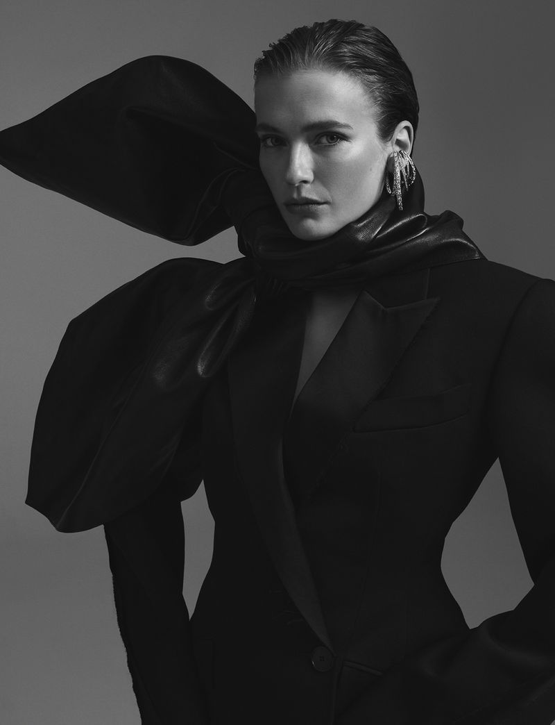 Monochrome portrait of a model wearing an oversized black blazer with dramatic puffed shoulders and statement earrings in a studio setting.