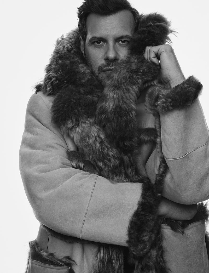 Portrait of Laurent Lafitte in a heavy fur-trimmed shearling coat against a plain white background for Numero Homme.