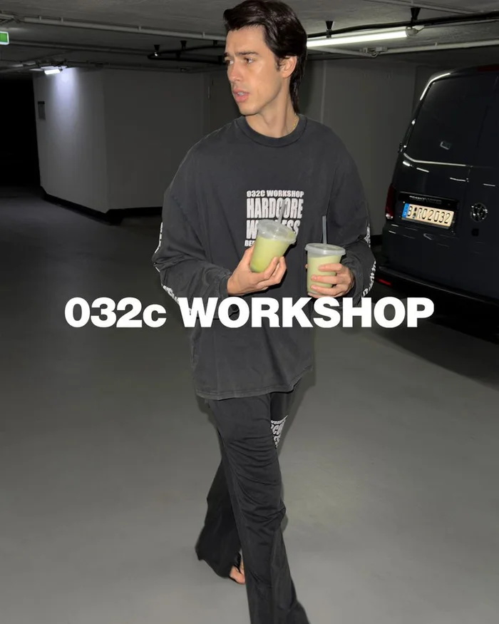 Bruno Sharif walking in an underground parking garage wearing a black 032c sweatshirt and holding two green drinks.