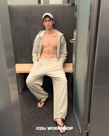 Model Bruno Sharif wearing beige sweatpants and an open zip hoodie on a bench for 032c Hardcore Wellness