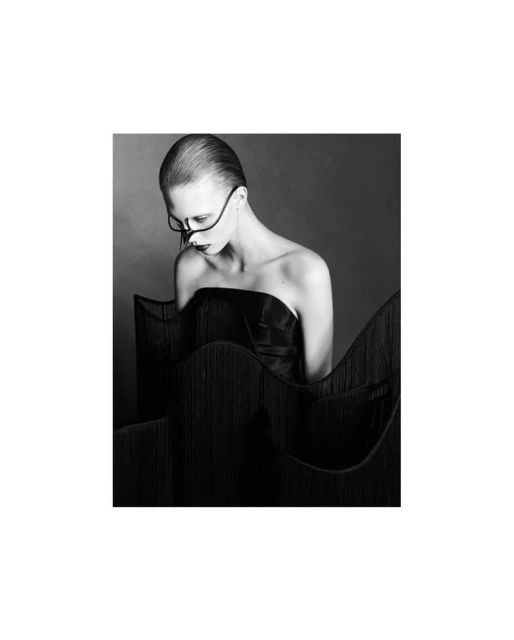 Monochrome portrait of an adult female model wearing strapless dress and elaborate face mask against a neutral grey background.