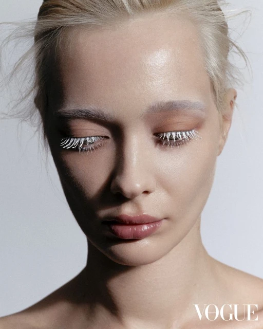 Close-up of a young woman with pale skin, white eyelashes and eyebrows, wearing light eyeshadow, and posing in a photo studio.