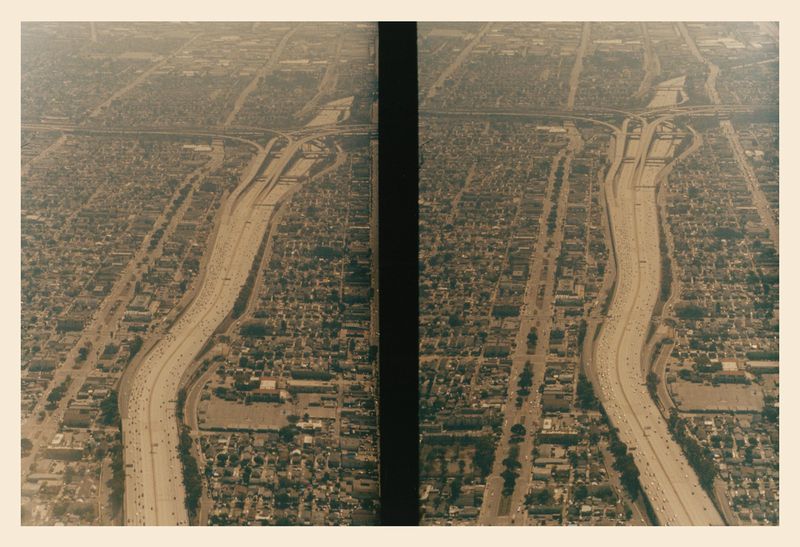 Aerial view of a dense urban area with a major highway system cutting through it, showing traffic and residential buildings.