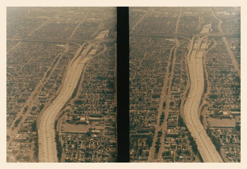 Aerial view of a dense urban area with a major highway system cutting through it, showing traffic and residential buildings.