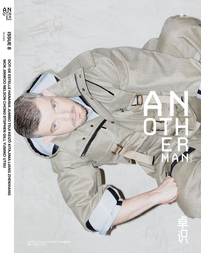Fashion editorial magazine cover featuring a reclining man in a plaid suit jacket and pants, posing indoors with clear magazine typography.