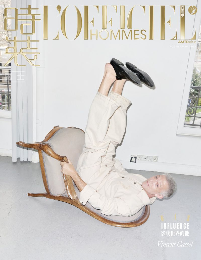 Upside-down cover shot of older male model Vincent Cassel for L'Officiel Hommes China, wearing loafers and relaxed beige suit in studio.