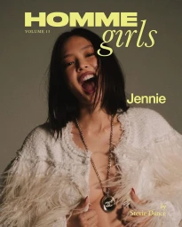 Jennie laughing wearing a white textured fringed jacket with a long pendant necklace against a neutral grey background