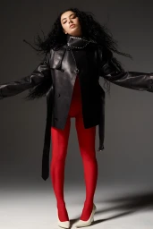 Charli XCX in a black leather jacket and red leggings against a grey background