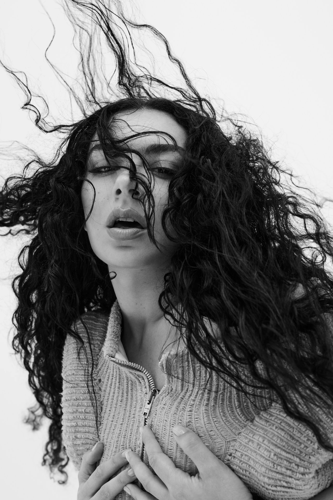 Portrait of Charli XCX with dark flowing hair in a textured top against a bright white background